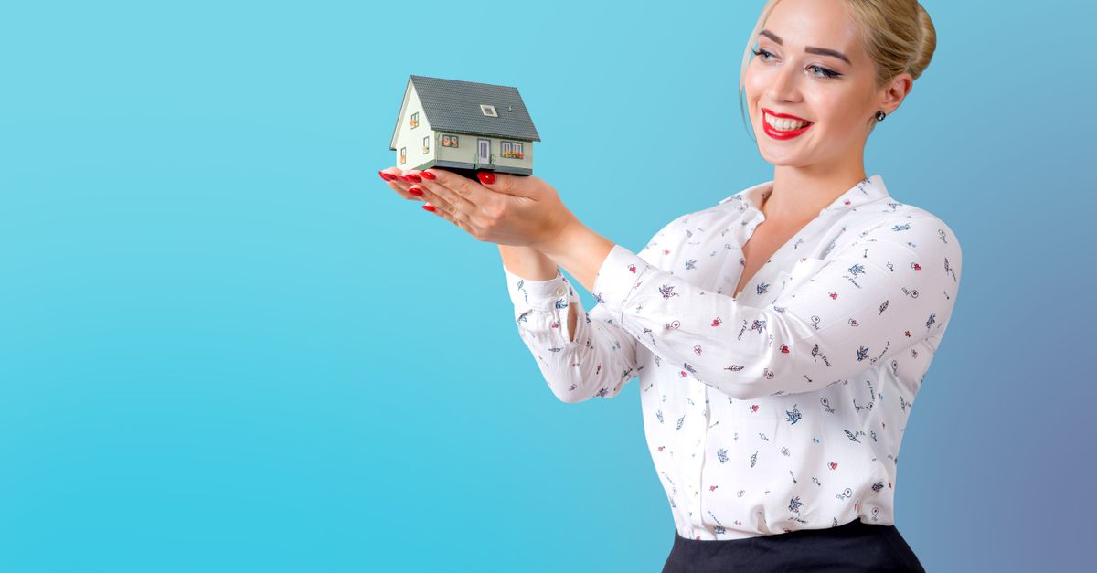 Professional woman in elegant attire holding a miniature house model, symbolizing real estate and home ownership.