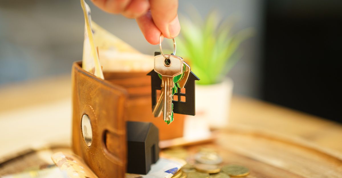 Close-up of hand holding a house key with a wallet and coins, symbolizing real estate investment.